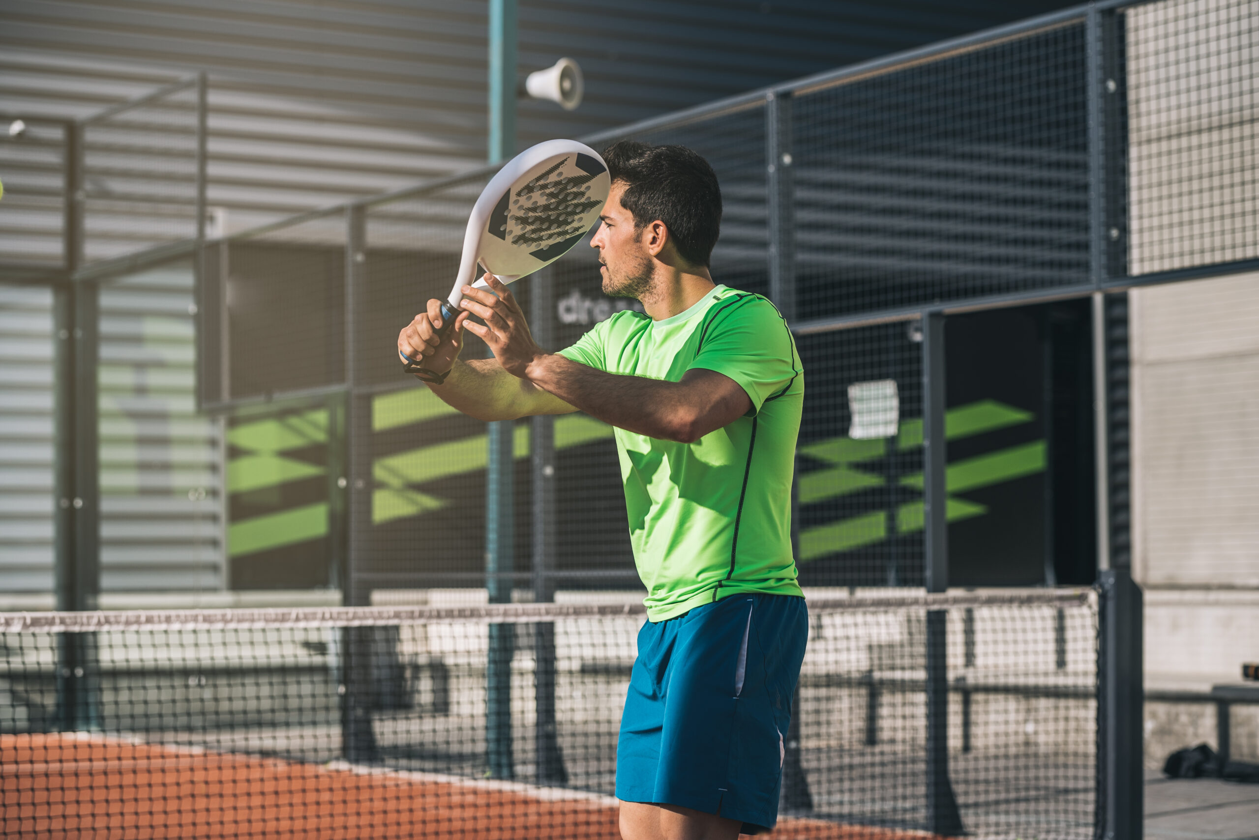 Man playing padel in a orange grass padel court outdoors behind the net